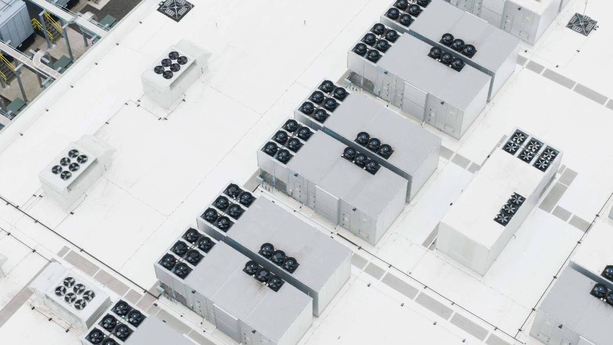 Aerial view of a white rooftop with multiple rectangular cooling units and rows of rooftop fans arranged across the surface.