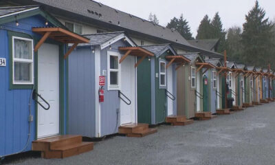Row of colorful small cottages with white doors, wooden steps, and string lights along a gravel lot.