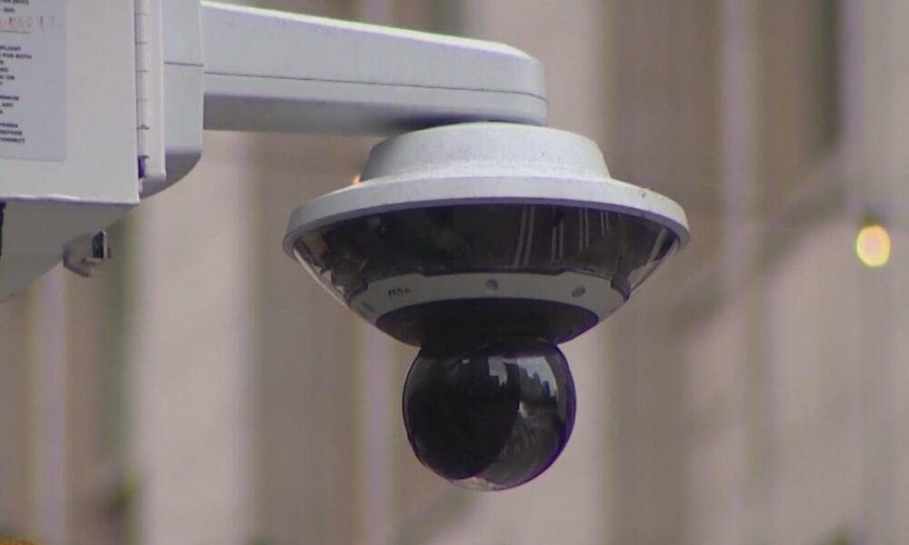 Outdoor dome security camera mounted on a bracket for exterior surveillance, glancing down over a street/area.