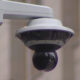 Outdoor dome security camera mounted on a bracket for exterior surveillance, glancing down over a street/area.