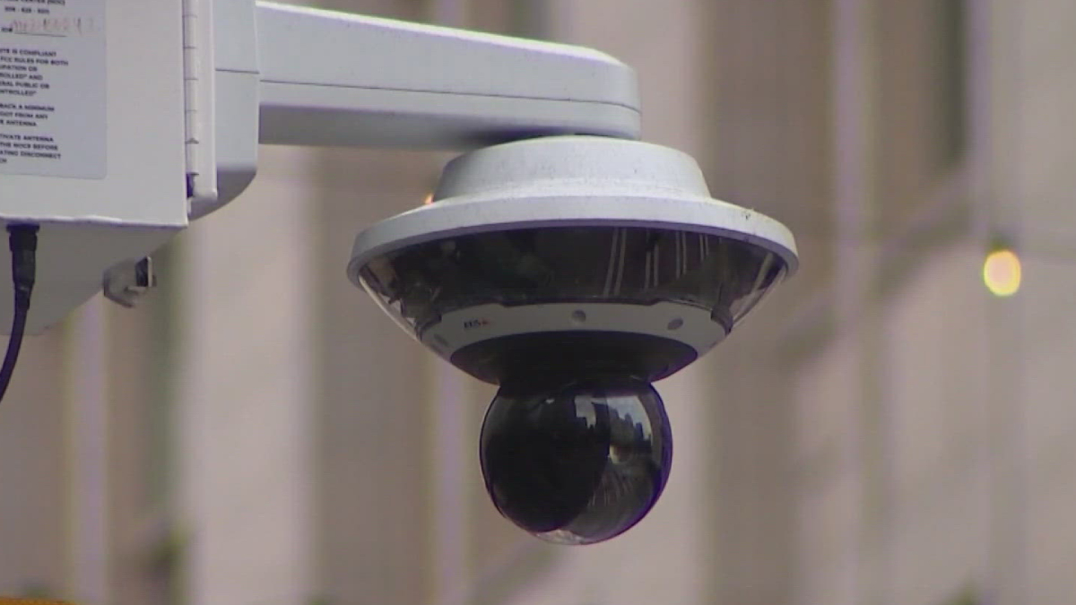 Outdoor dome security camera mounted on a bracket for exterior surveillance, glancing down over a street/area.