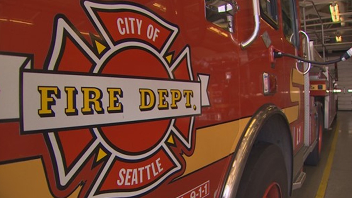 Red fire department fire engine with a Seattle Fire Dept logo and the words 'FIRE DEPT.' visible on the side, indoors in a station.