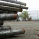 Stacked metal pipes tied together on a construction site with orange safety cones in the background.