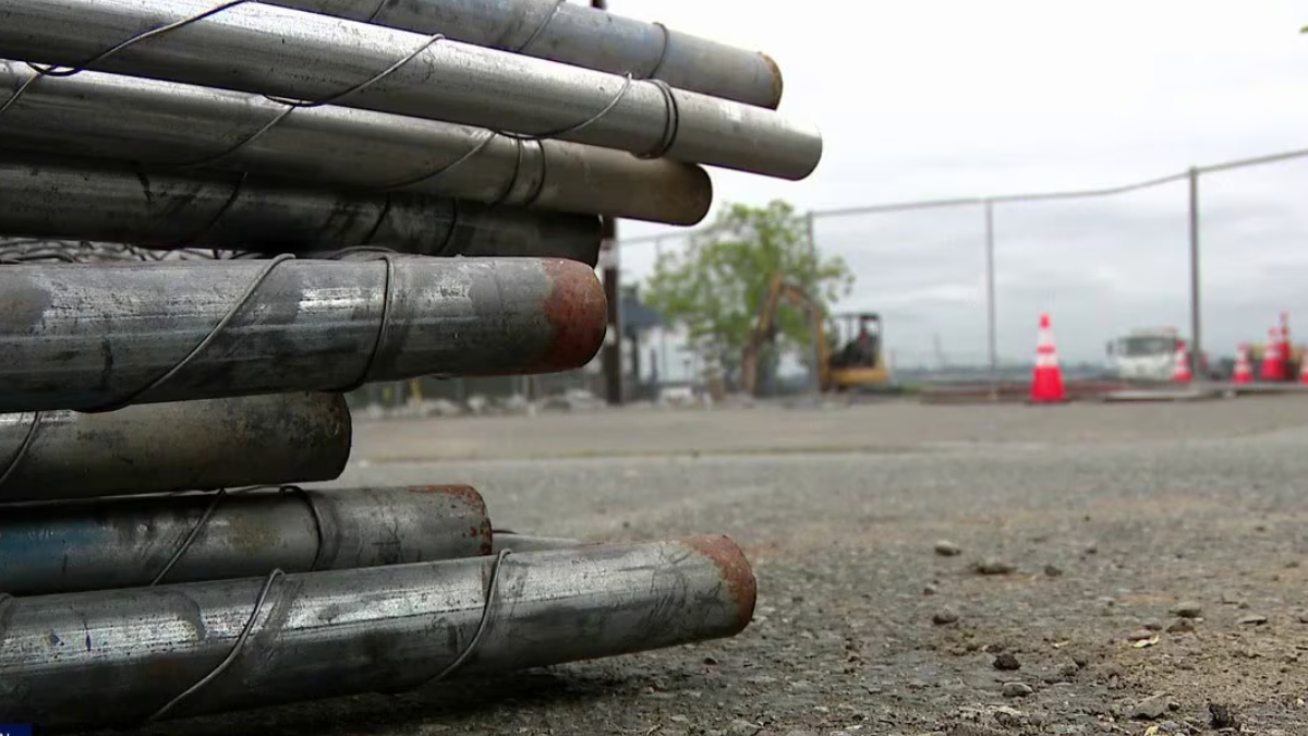 Stacked metal pipes tied together on a construction site with orange safety cones in the background.