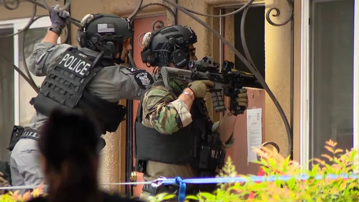 Two armed police officers in tactical gear aim rifles from a doorway, one with POLICE on his vest, preparing for a raid or standoff.