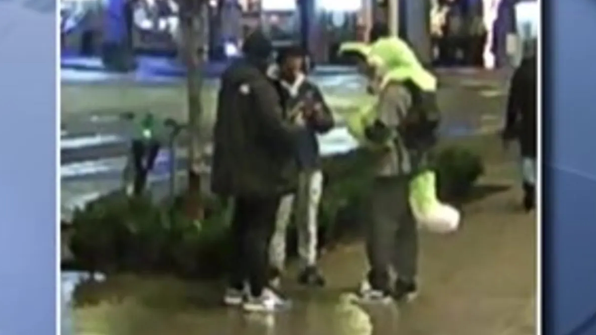 Three people stand on a wet city sidewalk, two in dark coats and sneakers, one in a bright neon jacket, chatting near a railing.