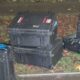 Assorted black hard protective cases on a grassy roadside with cables and tools spilling out nearby.