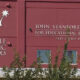 Exterior of a red Seattle Public Schools building featuring the John Stanford Center for Educational Excellence sign and the address 2445 Third Avenue South, with a tree partially obscuring the lower facade.