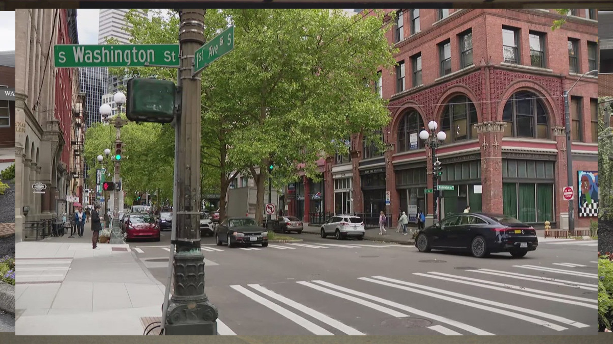 Intersection at S Washington St and 1st Ave S in a city, brick buildings, trees, crosswalks, and moving cars.