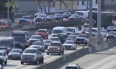 Heavy traffic on a multi-lane highway with concrete barriers and orange construction cones along the median edge.