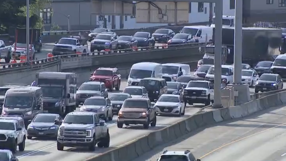 Heavy traffic on a multi-lane highway with concrete barriers and orange construction cones along the median edge.