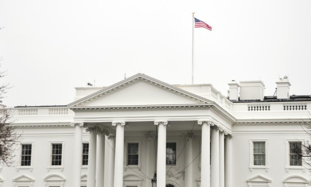 Front view of the White House with a neoclassical portico and an American flag on a flagpole