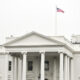 Front view of the White House with a neoclassical portico and an American flag on a flagpole