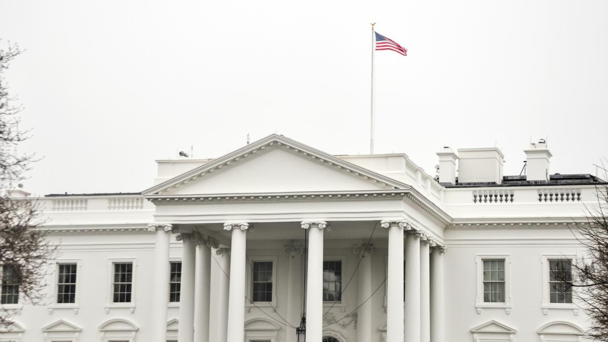 Front view of the White House with a neoclassical portico and an American flag on a flagpole