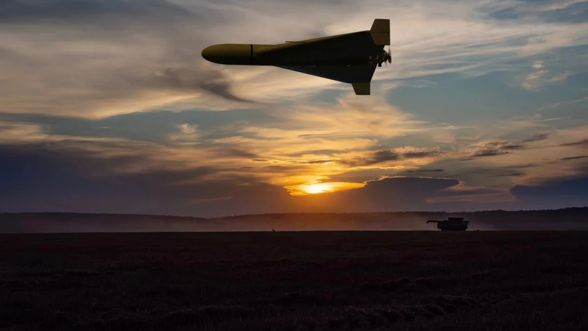 Unmanned military drone flies above a field at sunset; a distant tank sits on the ground.