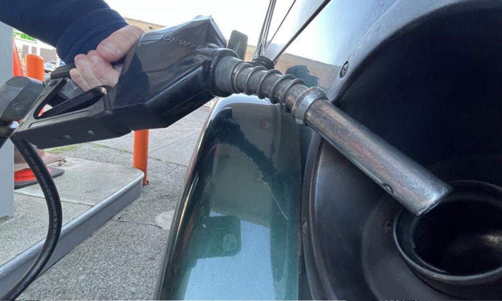 Close-up of a person pumping gas into a car, nozzle inserted into the fuel filler at a gas station.