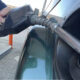 Close-up of a person pumping gas into a car, nozzle inserted into the fuel filler at a gas station.