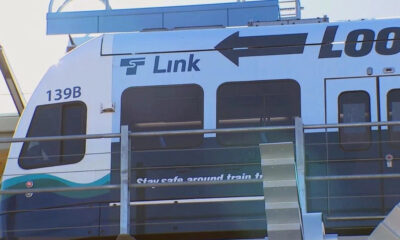 Front section of a blue-and-white passenger train with the word 'Link' and a large black arrow, partial '139B' number, and safety wording on the door area.