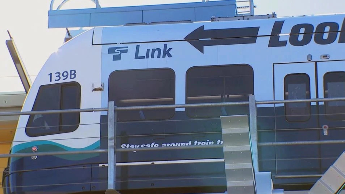 Front section of a blue-and-white passenger train with the word 'Link' and a large black arrow, partial '139B' number, and safety wording on the door area.