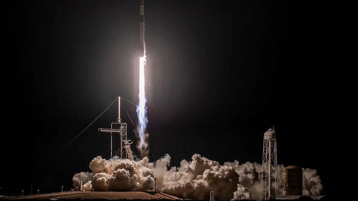 Rocket lifting off from a night launch pad, bright exhaust plume lighting the dark sky amid billowing smoke and dust.