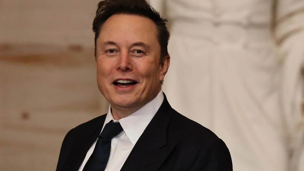 Smiling man in a dark suit and tie at a formal event, speaking or presenting.