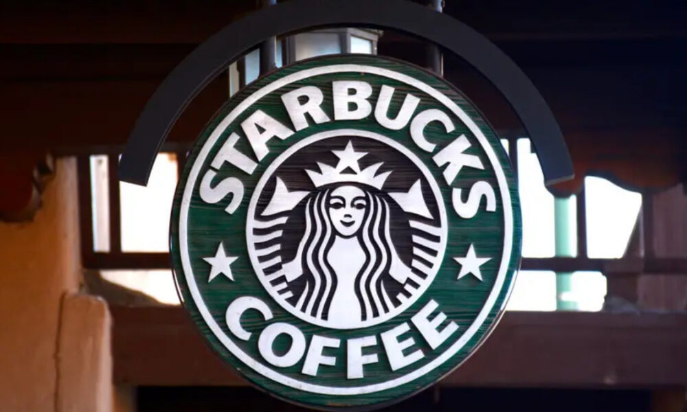 Circular Starbucks Coffee sign with green background and white siren logo hanging indoors/externally.