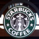 Circular Starbucks Coffee sign with green background and white siren logo hanging indoors/externally.