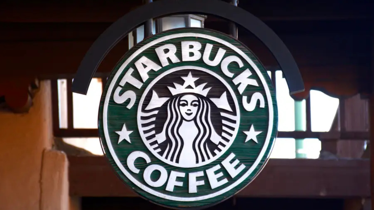 Circular Starbucks Coffee sign with green background and white siren logo hanging indoors/externally.