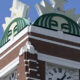 Brick clock tower with a large green circular emblem on top and a Roman numeral clock below.