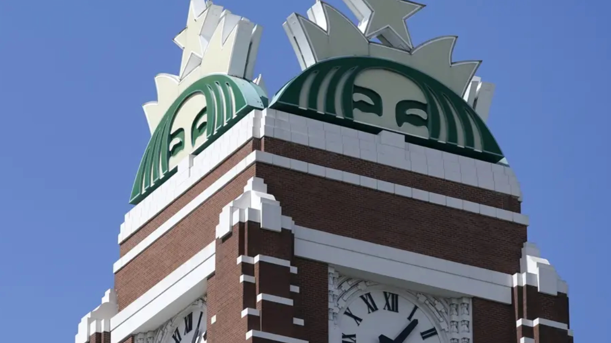 Brick clock tower with a large green circular emblem on top and a Roman numeral clock below.