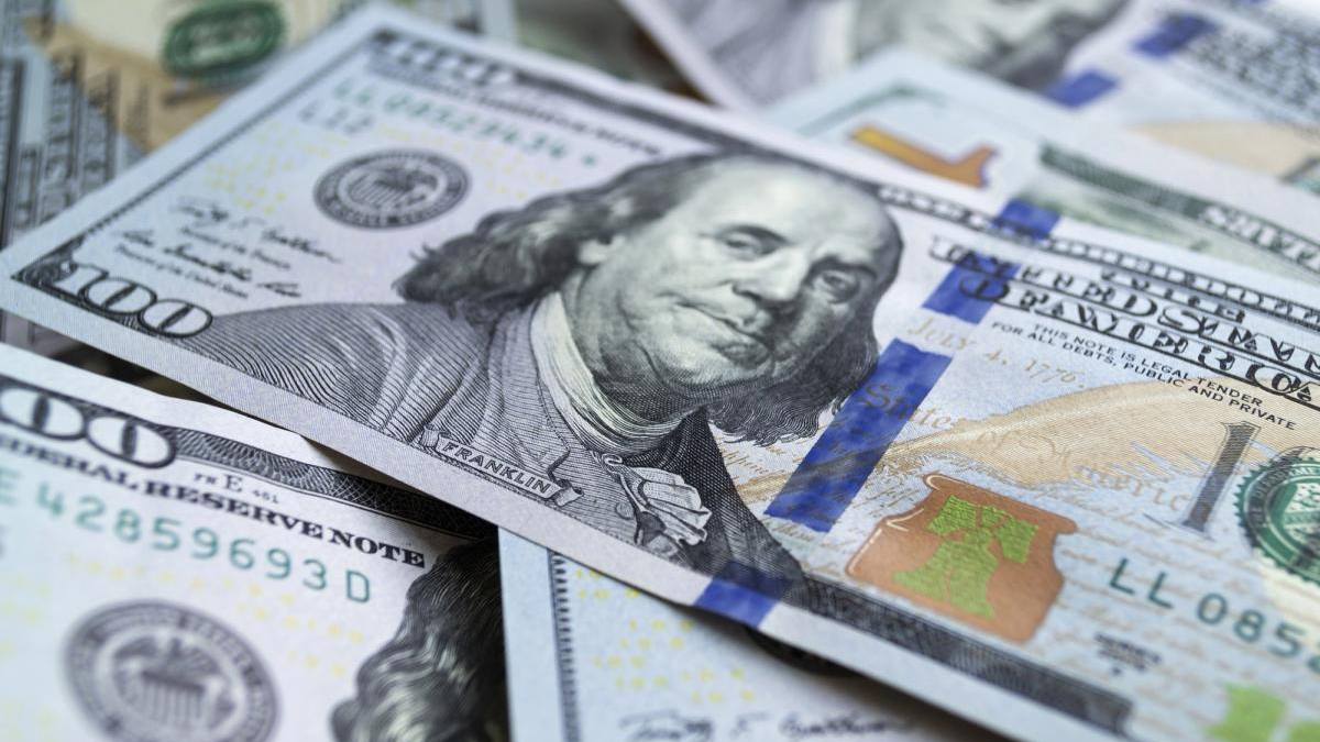 Close-up of multiple US $100 bills scattered on a surface, showing Benjamin Franklin's portrait and the note's design.