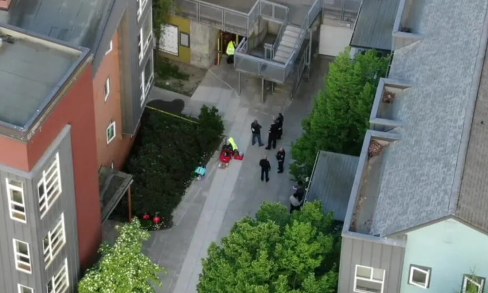 Aerial view of a courtyard between modern buildings with several people gathered, some in high-visibility clothing, near a stairwell.