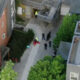 Aerial view of a courtyard between modern buildings with several people gathered, some in high-visibility clothing, near a stairwell.