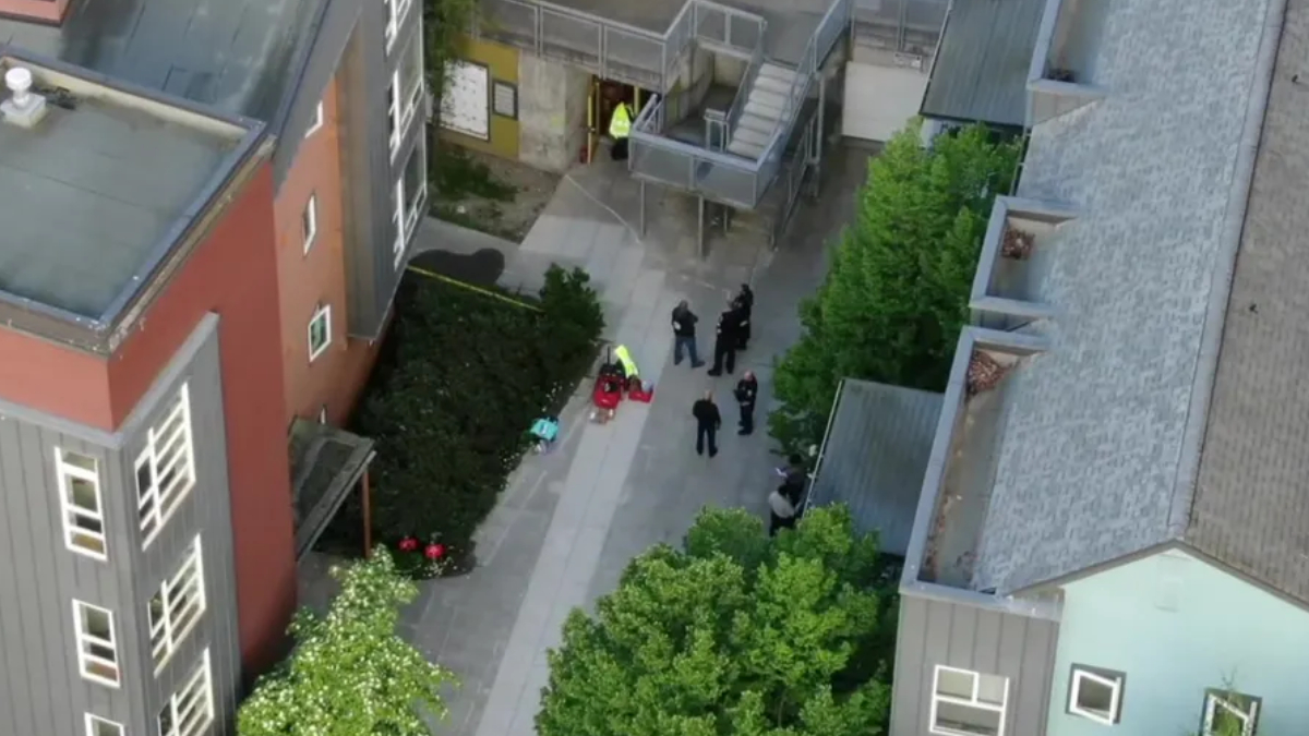 Aerial view of a courtyard between modern buildings with several people gathered, some in high-visibility clothing, near a stairwell.