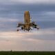 Large quadcopter UAV with orange landing gear hovering low over a grassy field under a cloudy sky