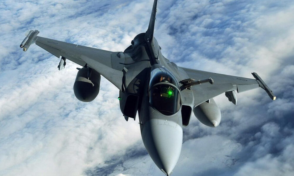 Front-on view of a sleek military fighter jet in mid-flight, nose toward the camera, flying above cloudy skies.