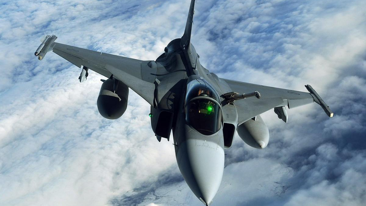 Front-on view of a sleek military fighter jet in mid-flight, nose toward the camera, flying above cloudy skies.