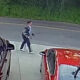 Man in a gray jacket walking on the sidewalk beside parked cars in a lot.