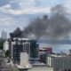 Smoke plume rising from a mid-rise building in a downtown waterfront district, indicating a fire nearby.