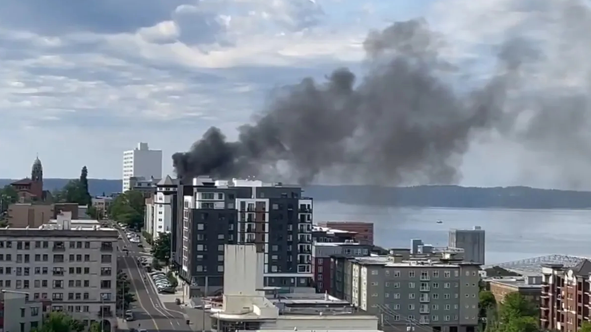 Smoke plume rising from a mid-rise building in a downtown waterfront district, indicating a fire nearby.