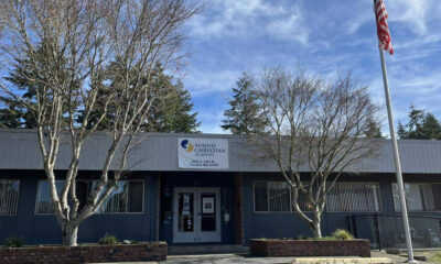 Front view of Sound Christian Academy building with a banner above the entrance, two leafless trees flanking the doors, and an American flag on a tall pole to the right.