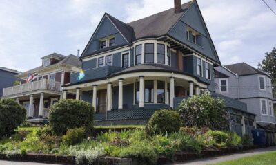 Blue Victorian-style house with wraparound porch and white columns, front garden in bloom, on a residential street