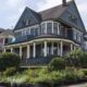 Blue Victorian-style house with wraparound porch and white columns, front garden in bloom, on a residential street