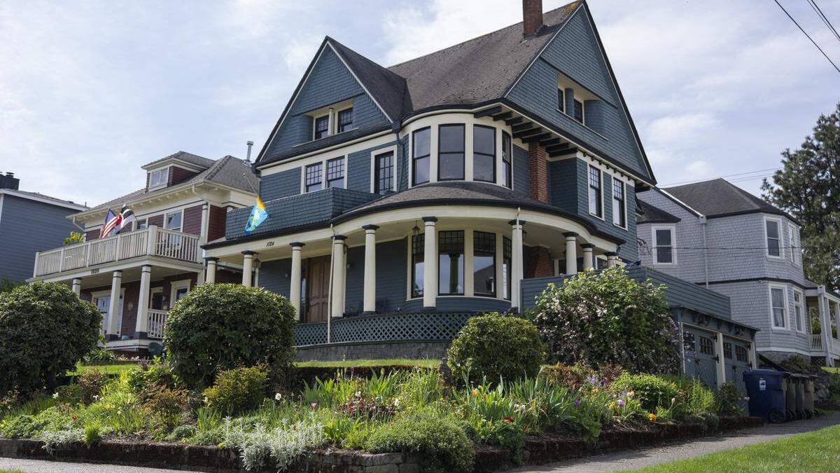 Blue Victorian-style house with wraparound porch and white columns, front garden in bloom, on a residential street