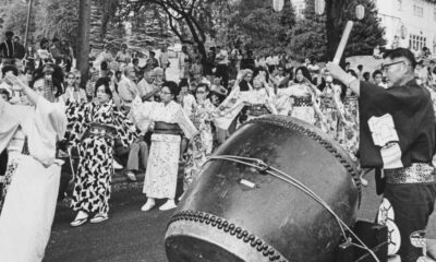 People in traditional kimonos dance around a large taiko drum during a festival parade outer edge of a crowd watching.