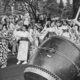 People in traditional kimonos dance around a large taiko drum during a festival parade outer edge of a crowd watching.