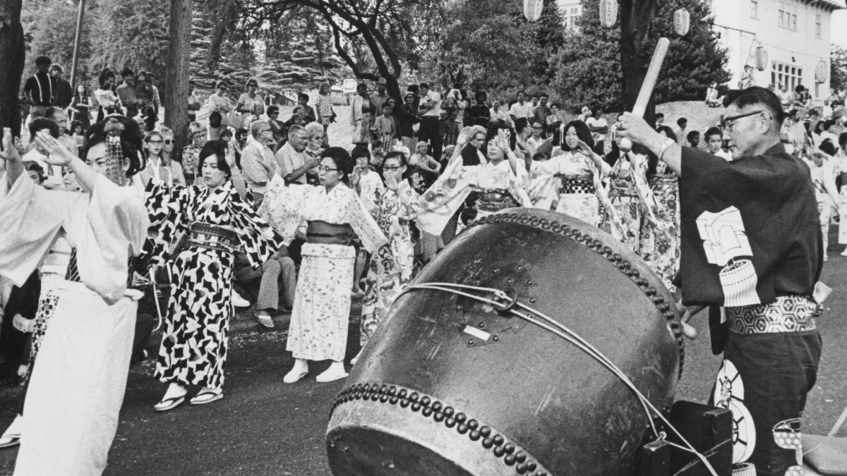 People in traditional kimonos dance around a large taiko drum during a festival parade outer edge of a crowd watching.