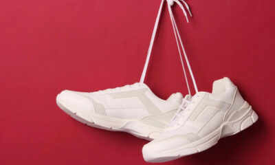 Pair of white sneakers suspended by their laces against a red background.