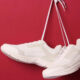 Pair of white sneakers suspended by their laces against a red background.