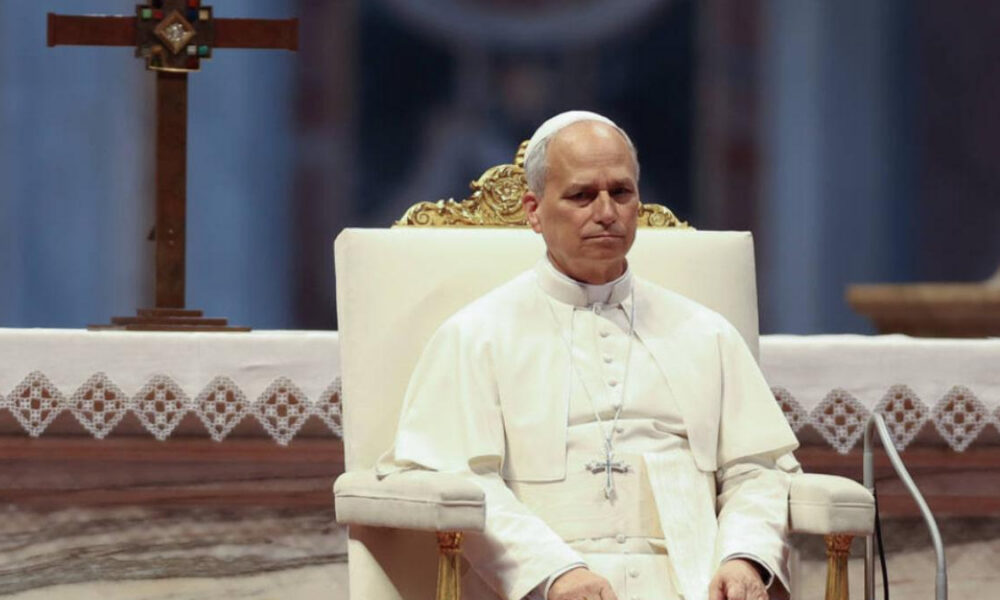Pope in white robes sitting on an ornate chair in a church setting with an altar behind him